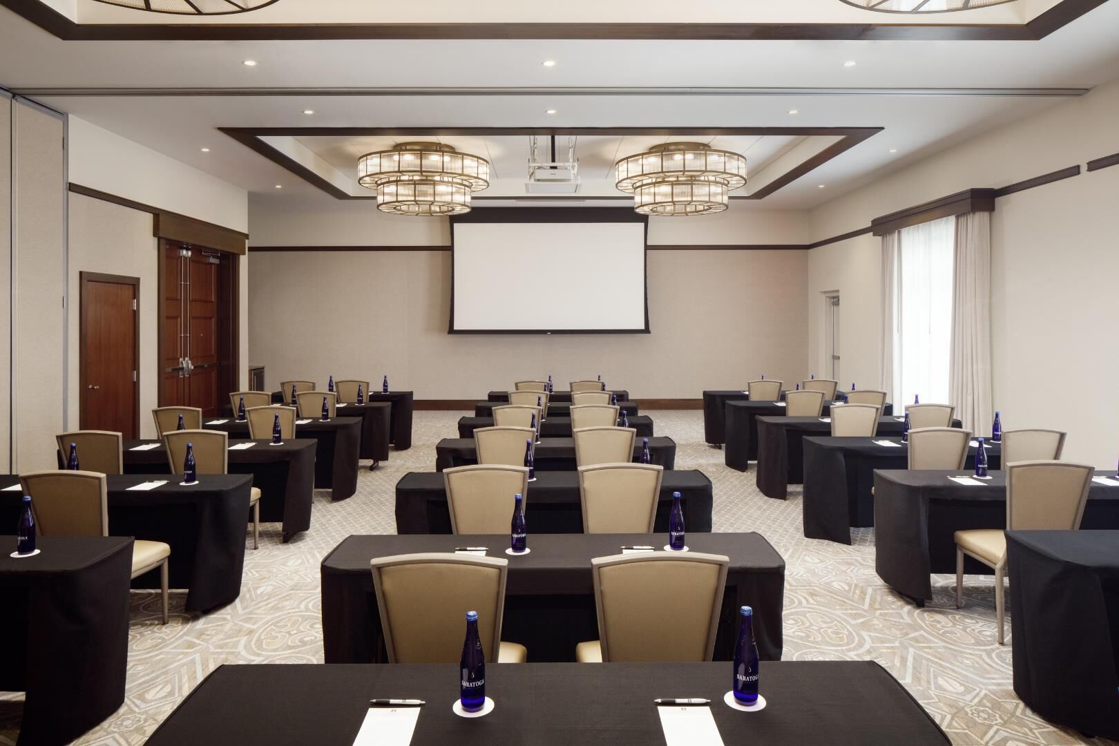 A conference room with multiple tables, chairs, and a projector screen.
