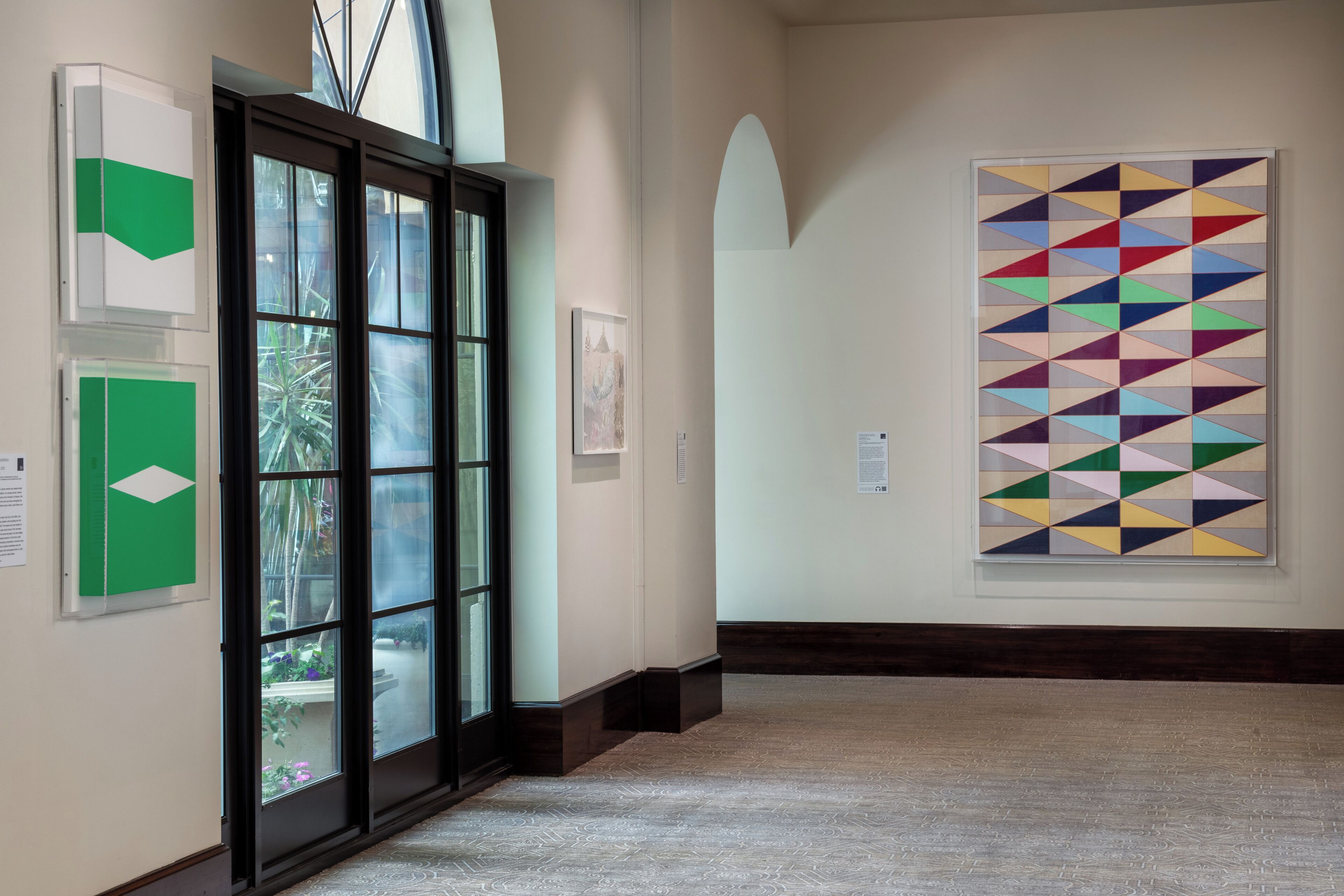 Ein Flur mit Kunstinstallationen, einer Glastür, die auf einen Balkon führt, und einem großen geometrischen Gemälde an der Wand.