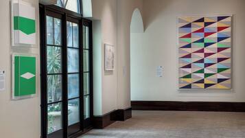 A hallway with art installations, a glass door leading to a balcony, and a large geometric painting on the wall.