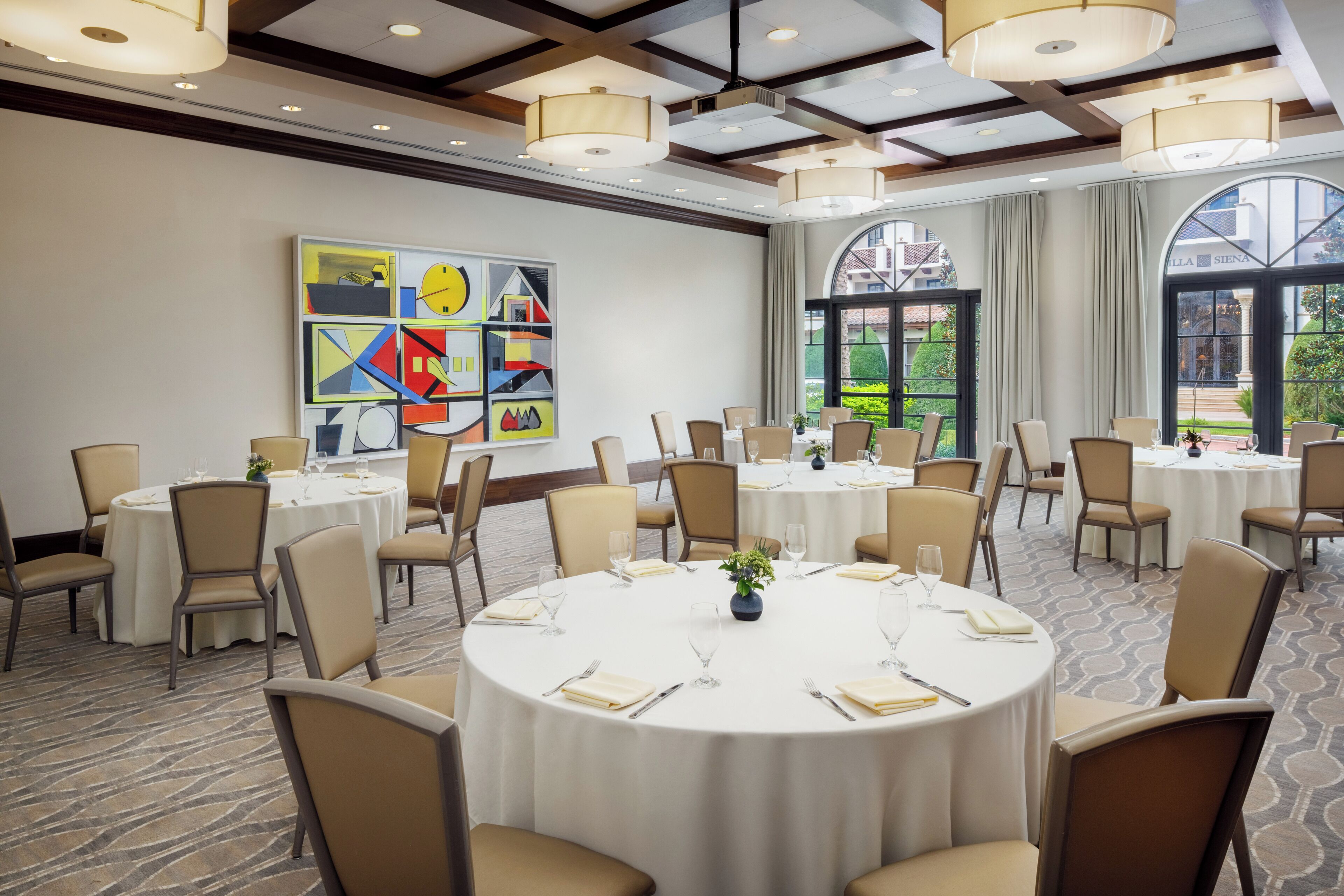 A conference room with round tables, beige chairs, and a large abstract painting on the wall.