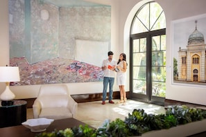 A room with a large abstract painting, a model of a building, and a view through a large window.