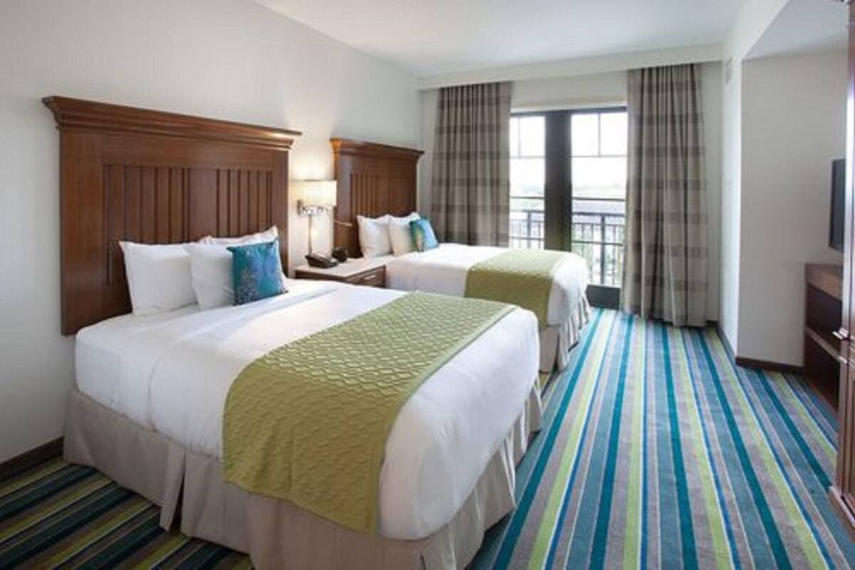 A hotel room with two beds, a wooden headboard, a striped carpet, and a window with curtains.