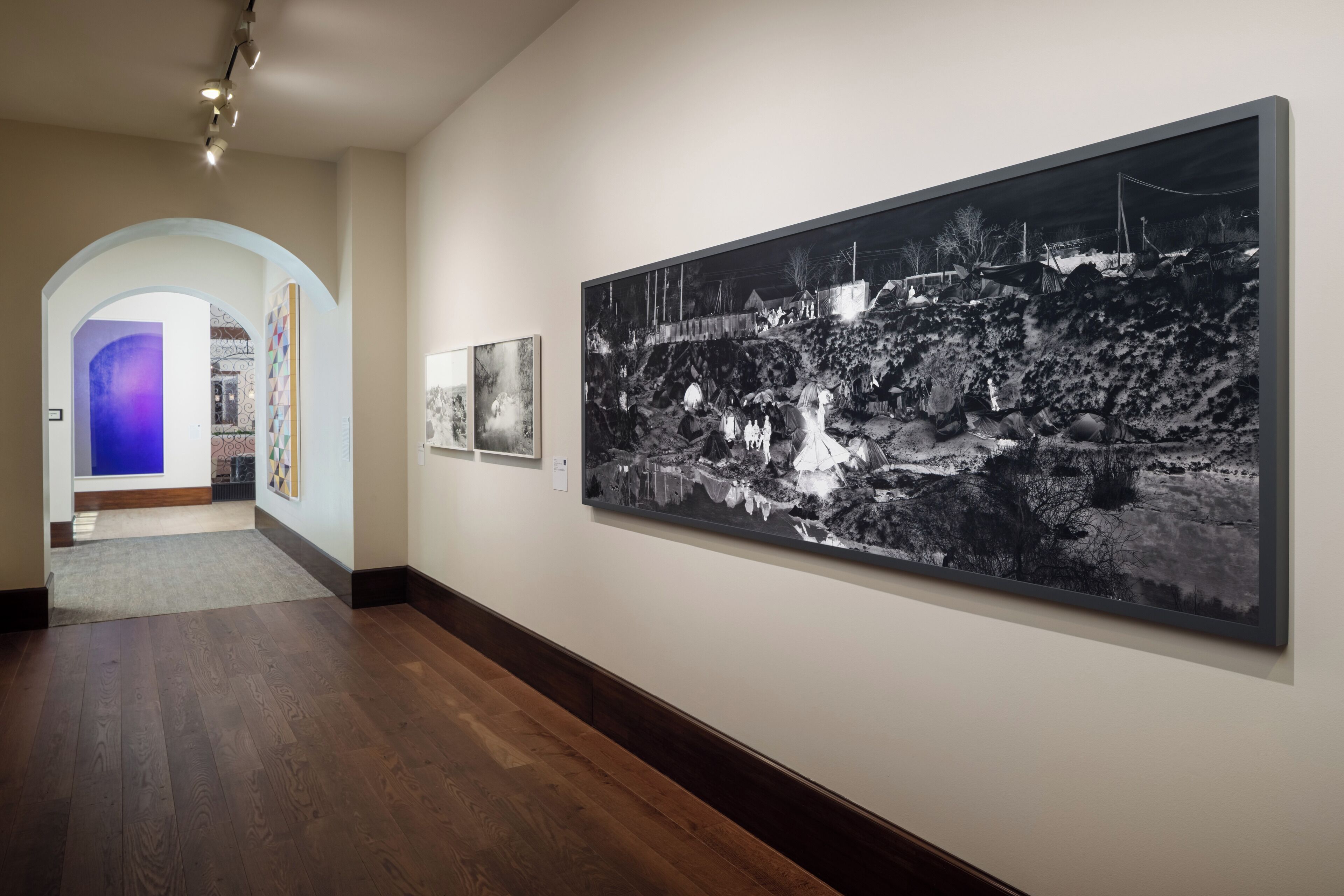 Une galerie d’art où l’on peut admirer une grande photographie en noir et blanc accrochée au mur, ainsi qu’un parquet en bois et un couloir agrémenté d’une arche illuminée de lumière bleue.