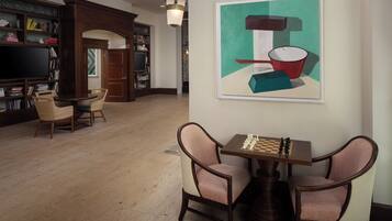 A spacious living room with a wooden floor, a bookshelf, a television, and a chess table.
