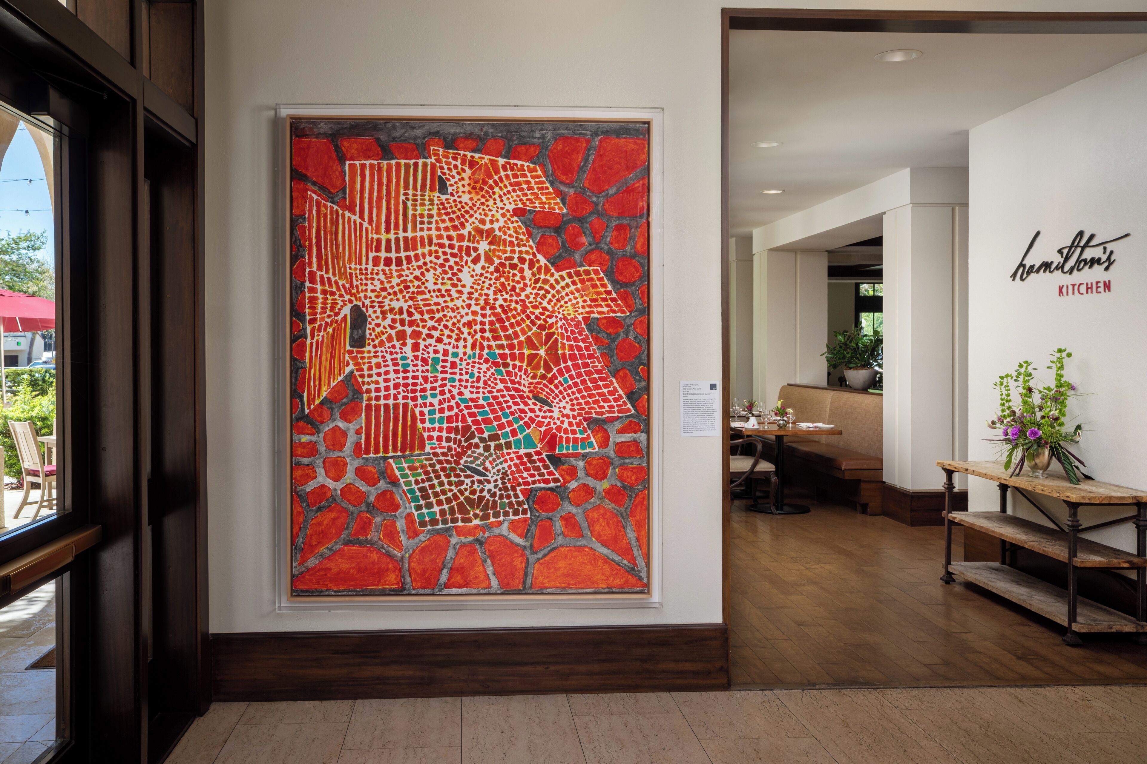 A modern interior with a large abstract art piece, a wooden bench, and a sign for Hamilton's Kitchen.