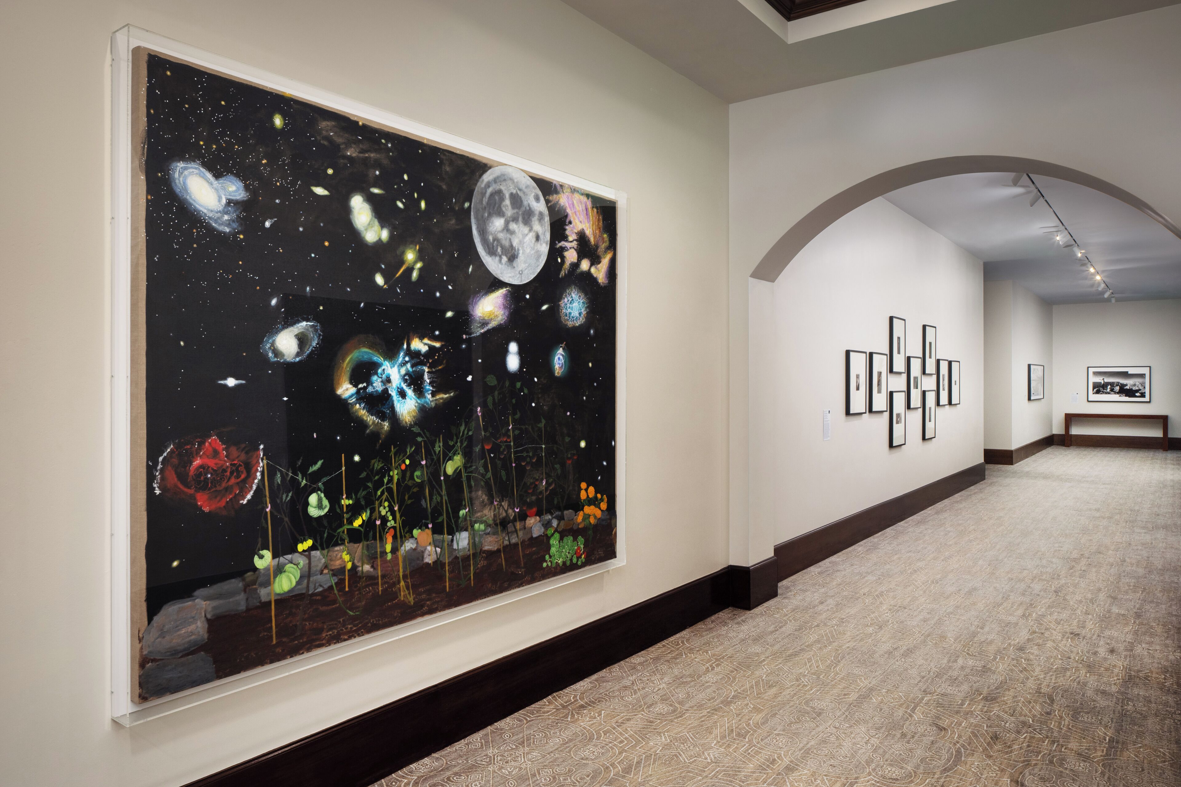 Una amplia galería de arte con un cuadro de gran tamaño que representa una escena cósmica en la pared, una alfombra estampada y obras de arte enmarcadas adornando las paredes.