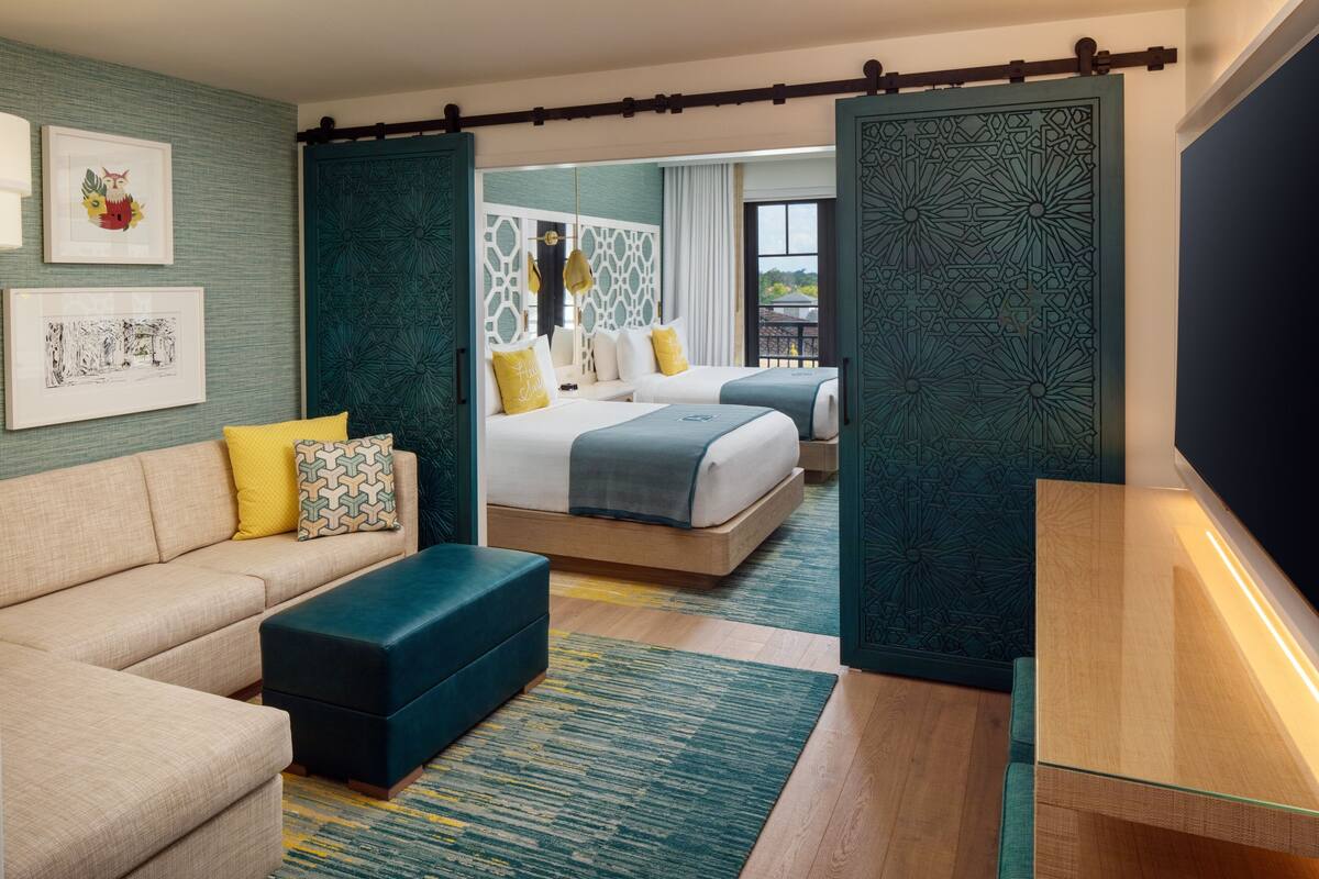 A modern hotel room with a sofa, two beds, a large window, and decorative wall art.