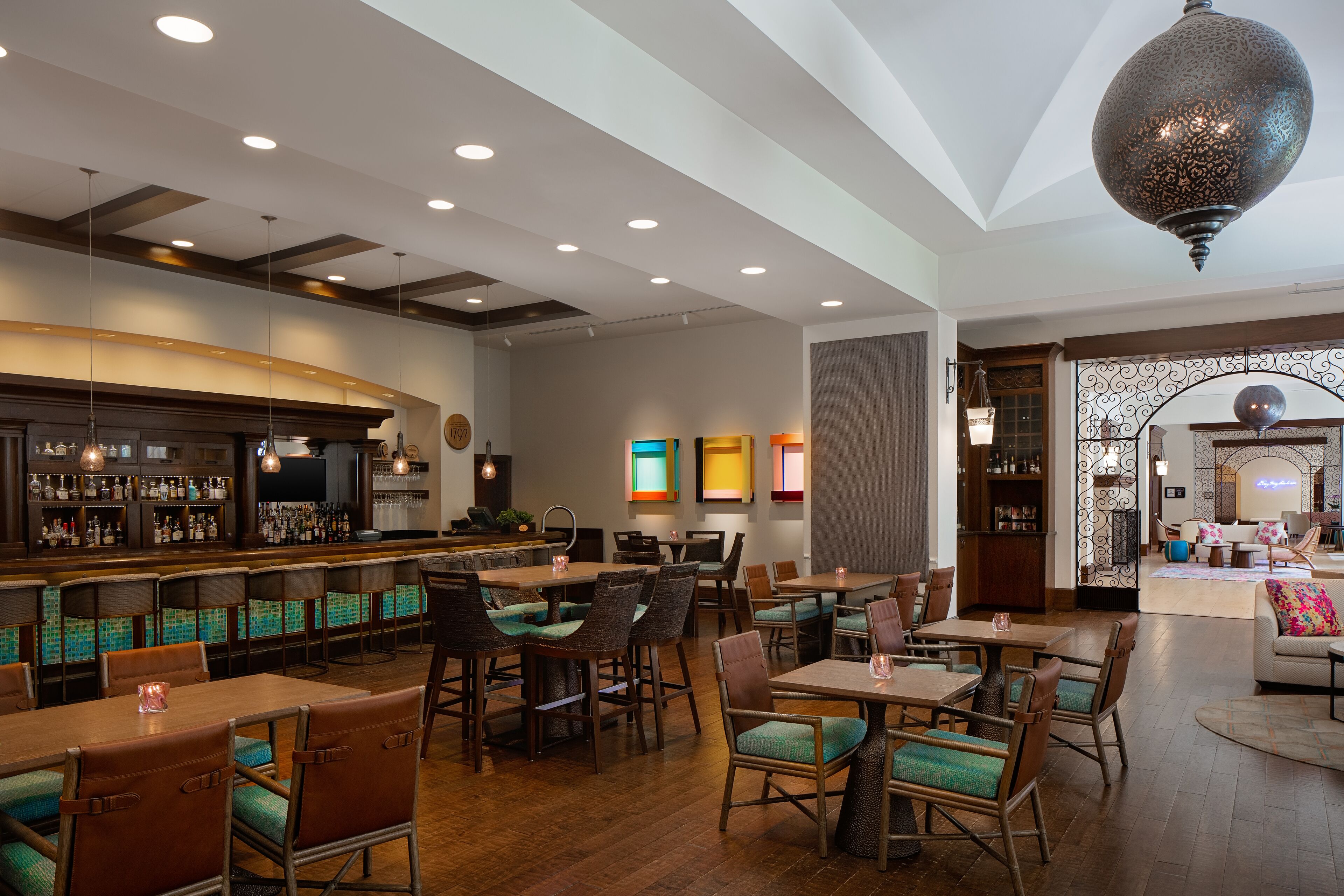 A restaurant with a bar area, wooden tables and chairs, and a decorative hanging light fixture.