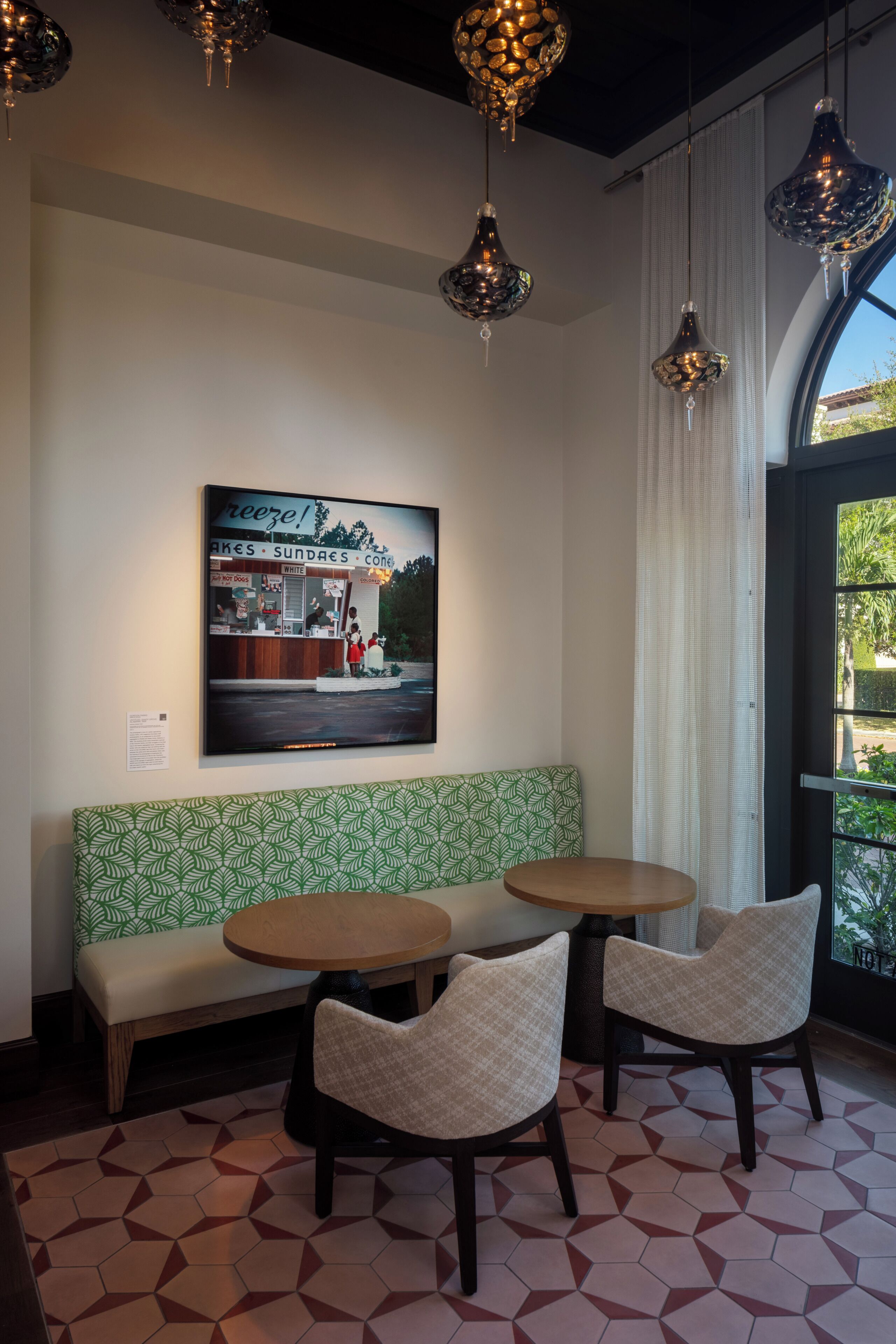 A seating area with a green patterned bench, two round tables, and hanging pendant lights.