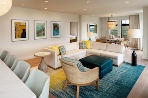 A modern hotel room with a living area, a dining table, and a large window.