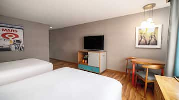 Ein Hotelzimmer mit zwei Betten, einem Fernseher, einem kleinen Tisch mit Stühlen und einer Kommode mit Schubladen.