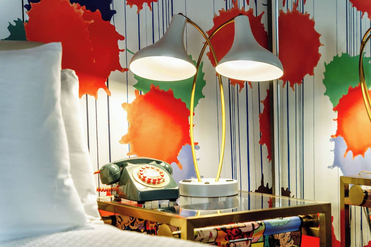 A room with a bed, a desk with a telephone, and a lamp.