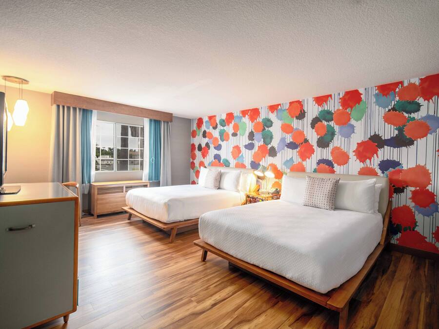 Een hotelkamer met twee bedden, een bureau, een televisie en een raam met gordijnen.