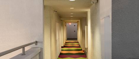 A hallway with a colorful zigzag carpet, white walls, and a railing on the left.