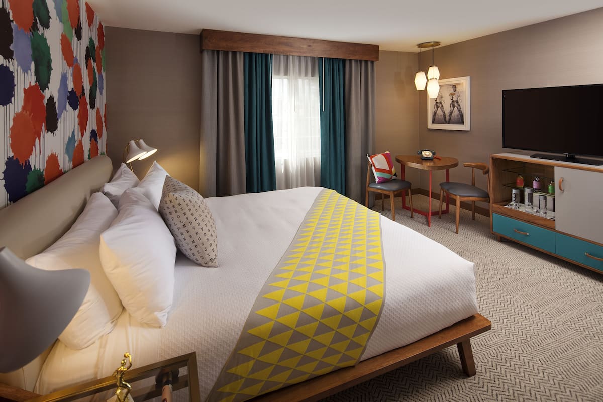 A hotel room with a bed, a desk, a chair, a television, and a minibar.