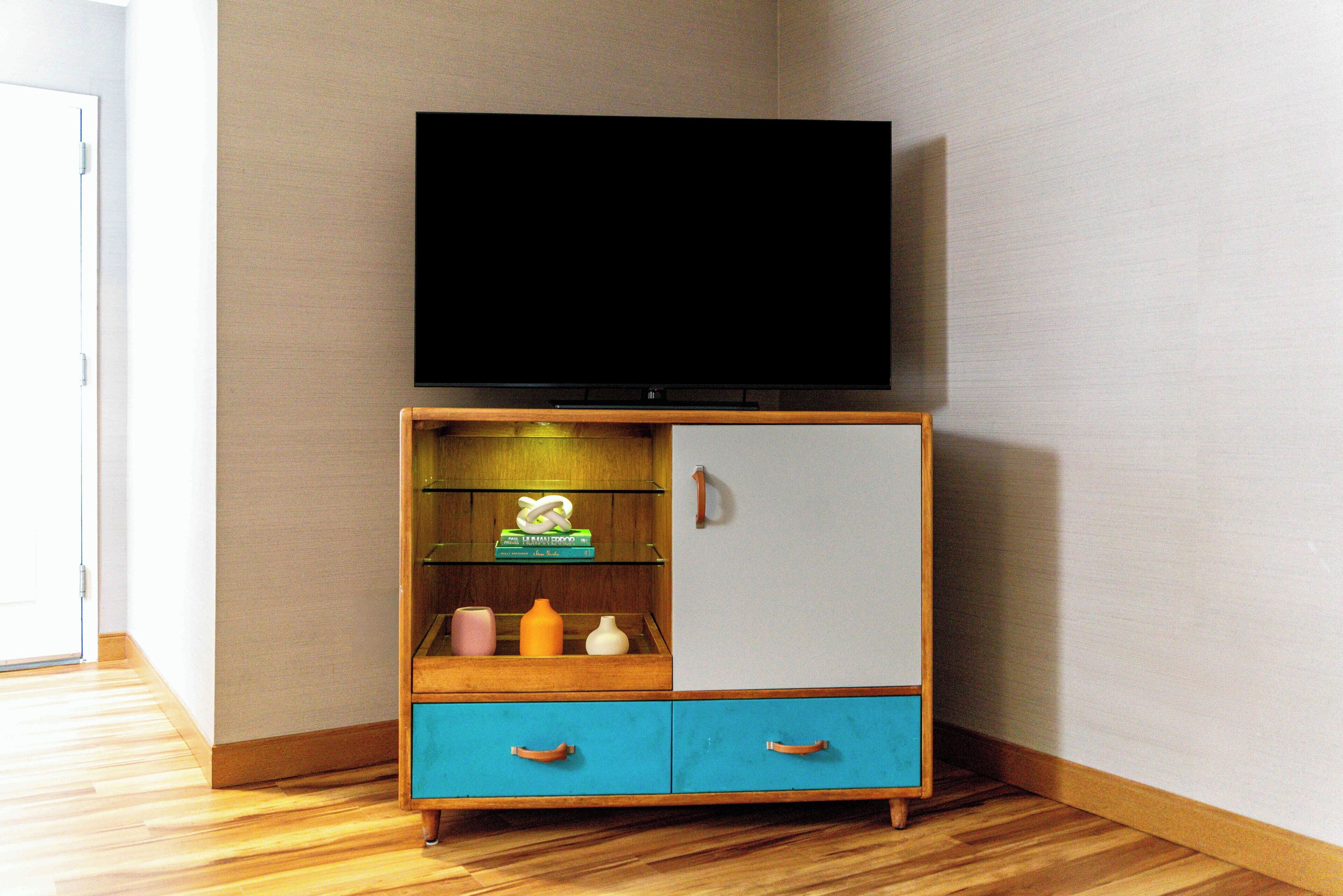 Una habitación de esquina con un armario de madera, un televisor encima y una puerta a la izquierda.