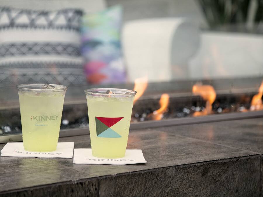 Two glasses of a yellow beverage on a stone surface with a fire in the background.