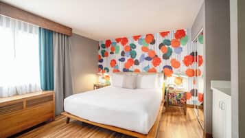 Un dormitorio moderno con una cama de madera, un ventanal con cortinas, un mural de colores y una mesita de noche con lámpara.