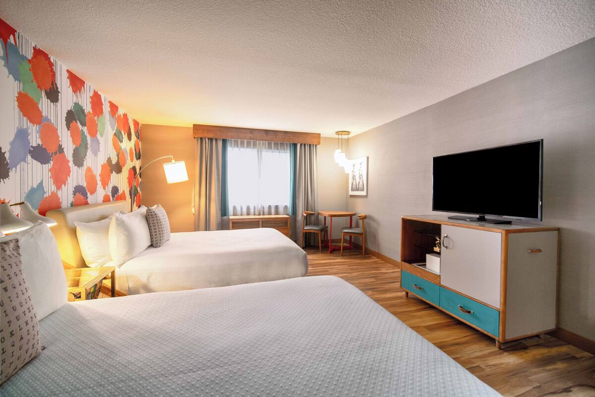 A hotel room with two beds, a TV, a desk with a chair, and a window with curtains.