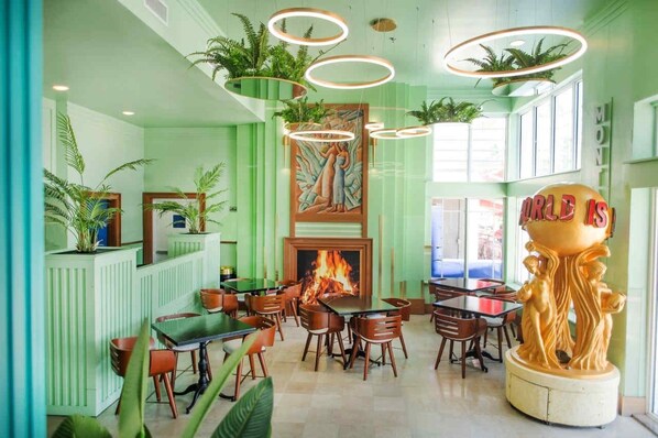 A restaurant with a green color scheme, wooden furniture, and a central fire feature.