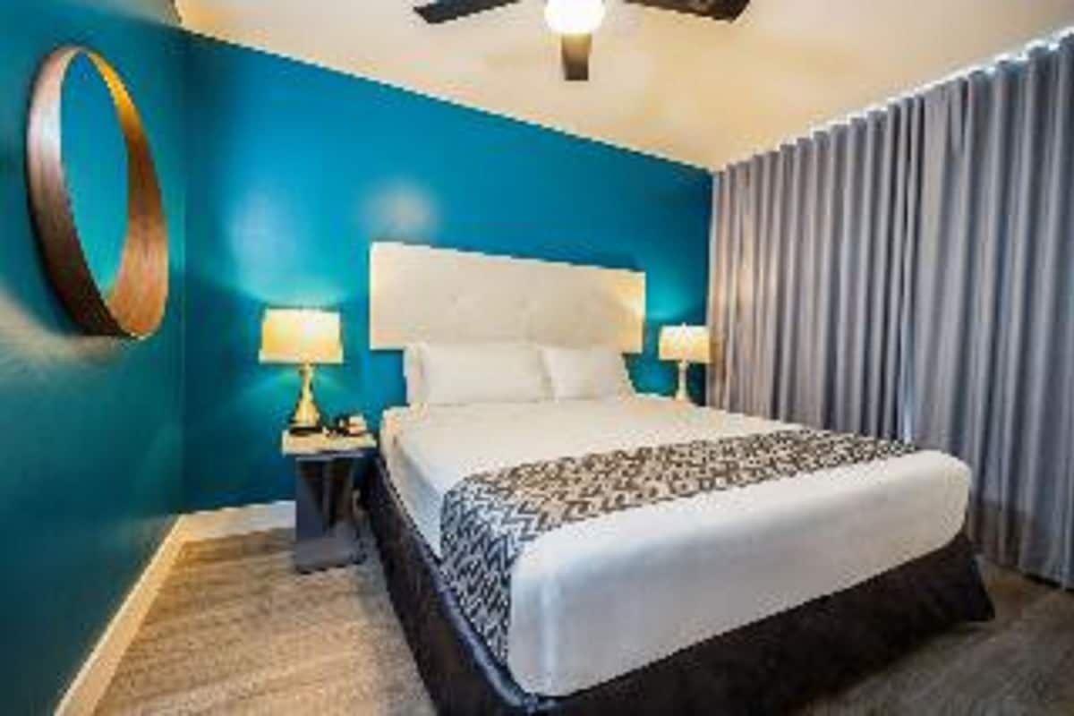 A hotel room with a large bed, a ceiling fan, and a nightstand with a lamp.
