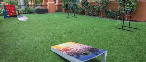 A courtyard with artificial grass, a table with a tropical print, and a small play area with a ball rack.
