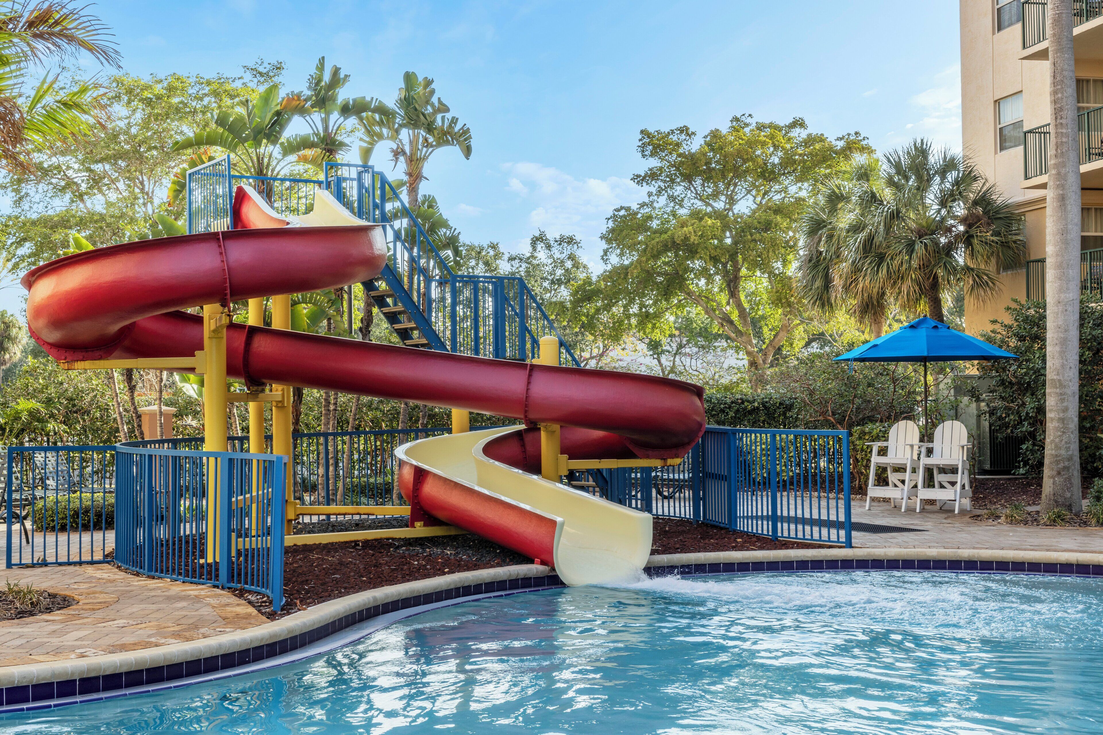 Un área de piscina con tobogán acuático, piscina y zona de estar con sillas y una mesa.