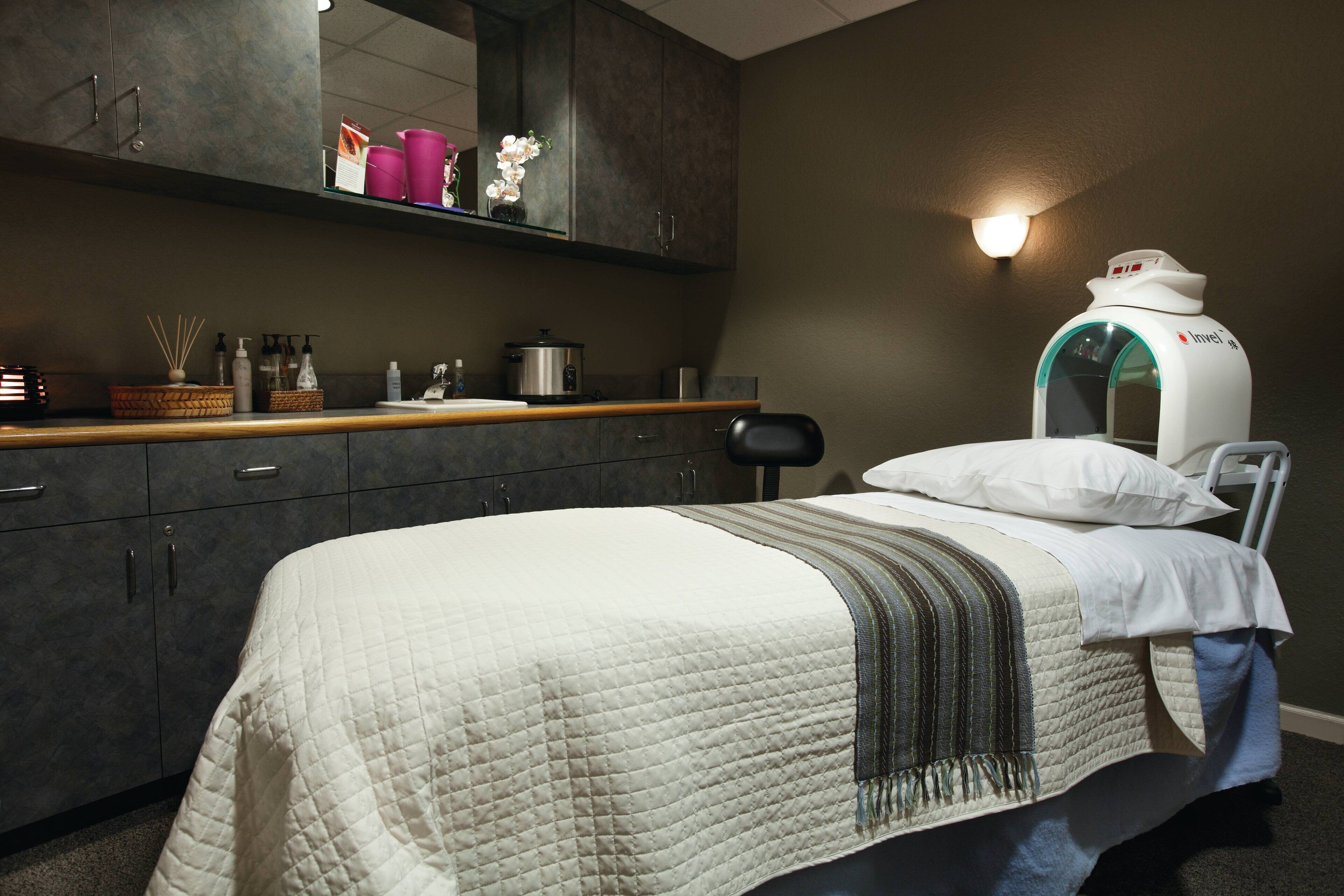 A bedroom with a bed, a bedside table, a mirror, and a wall-mounted device.
