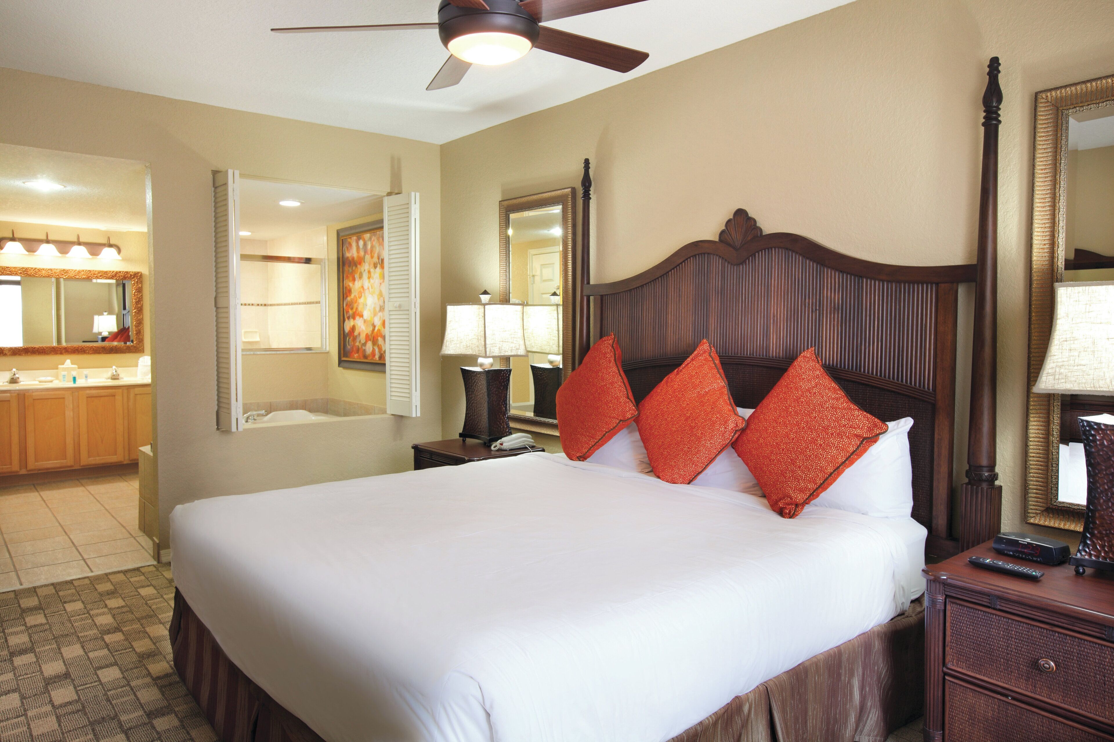 A hotel room with a large bed, a wooden headboard, two bedside lamps, a nightstand, and a ceiling fan.