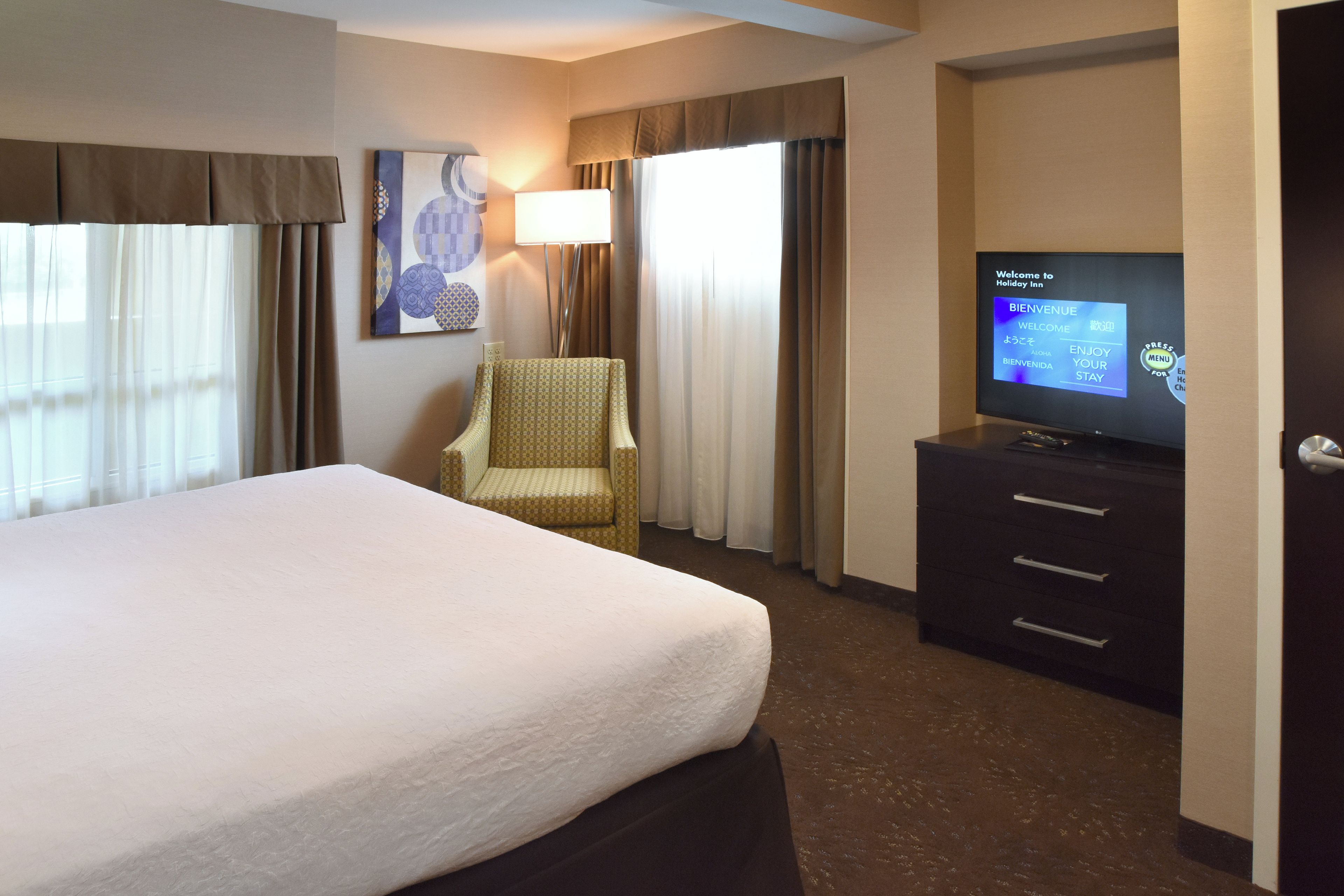 A hotel room with a bed, a television, a chair, and a desk with drawers.