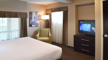 A hotel room with a bed, a television, a chair, and a desk with drawers.