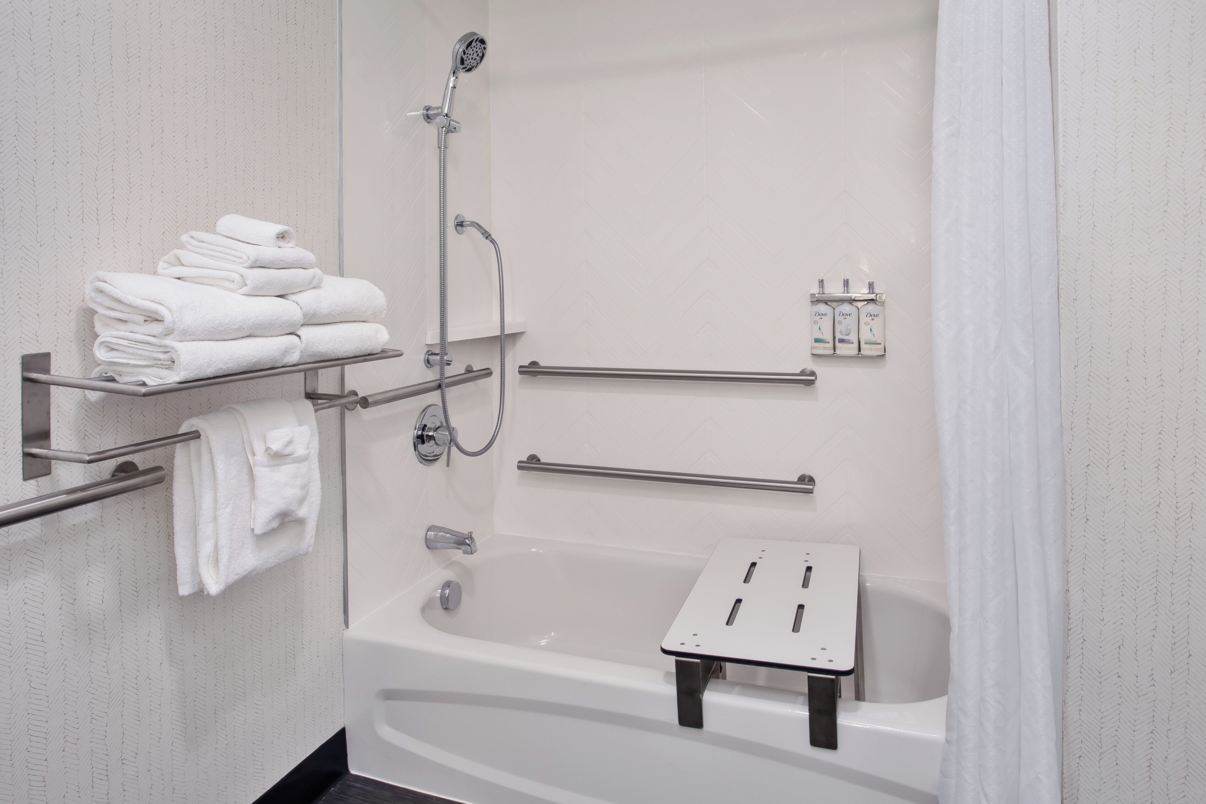 A modern bathroom with a bathtub, a shower, a towel rack with folded towels, and a soap dispenser.