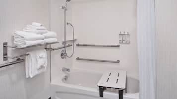 A modern bathroom with a bathtub, a shower, a towel rack with folded towels, and a soap dispenser.