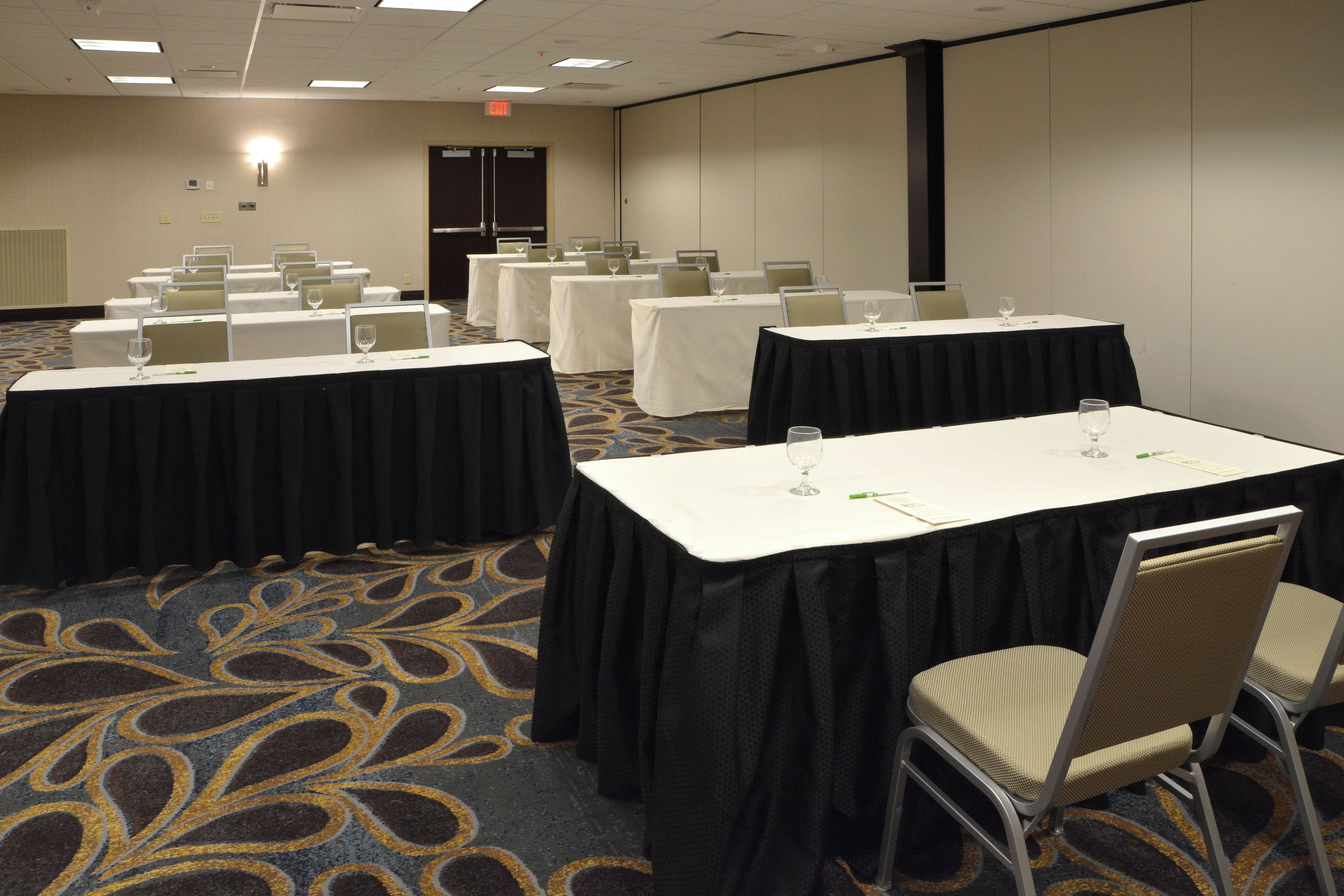 A conference room with multiple tables, each with a white tablecloth and a glass of water.
