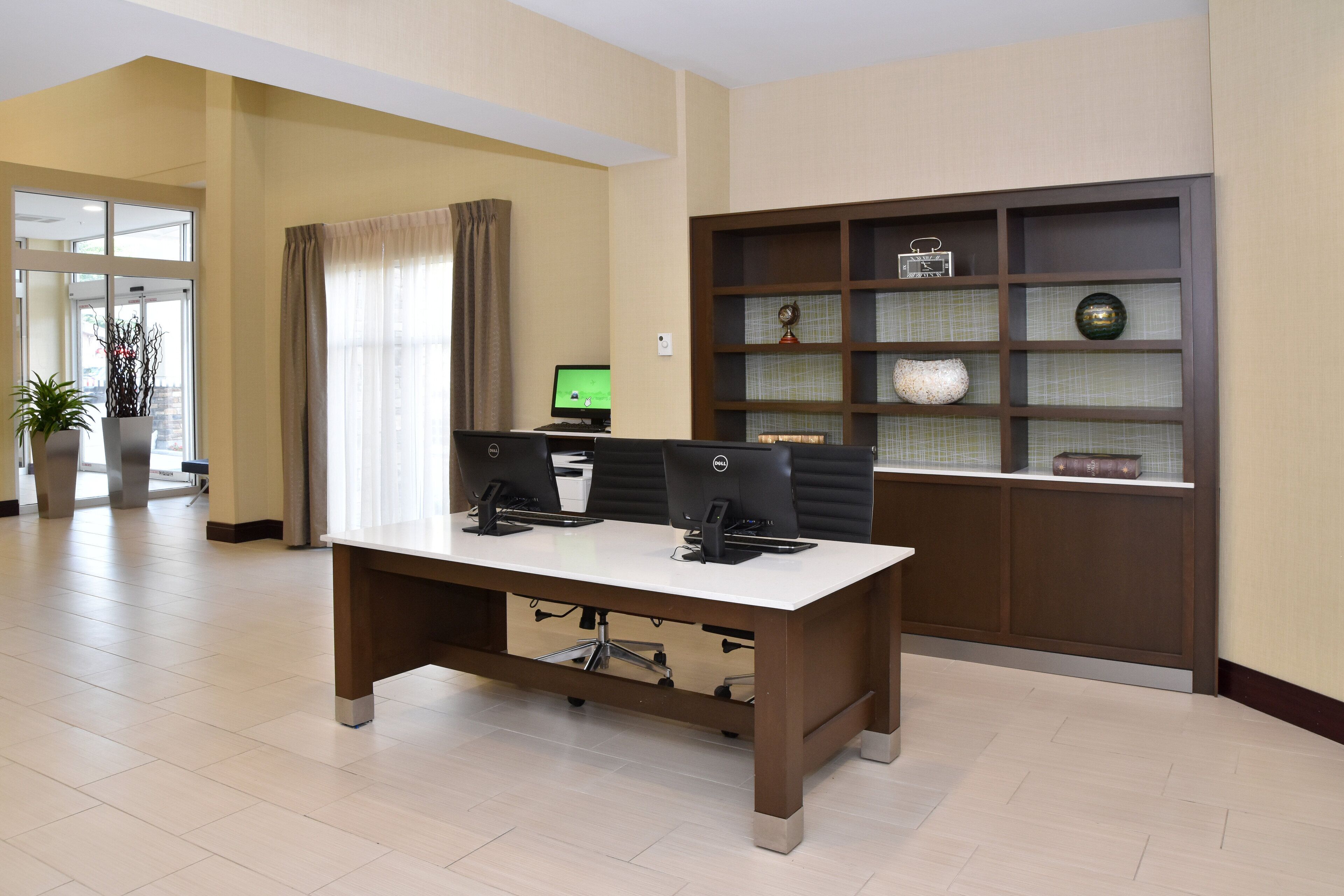 A conference room with a large table, two computer monitors, and a bookshelf with decorative items.