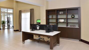 A conference room with a large table, two computer monitors, and a bookshelf with decorative items.