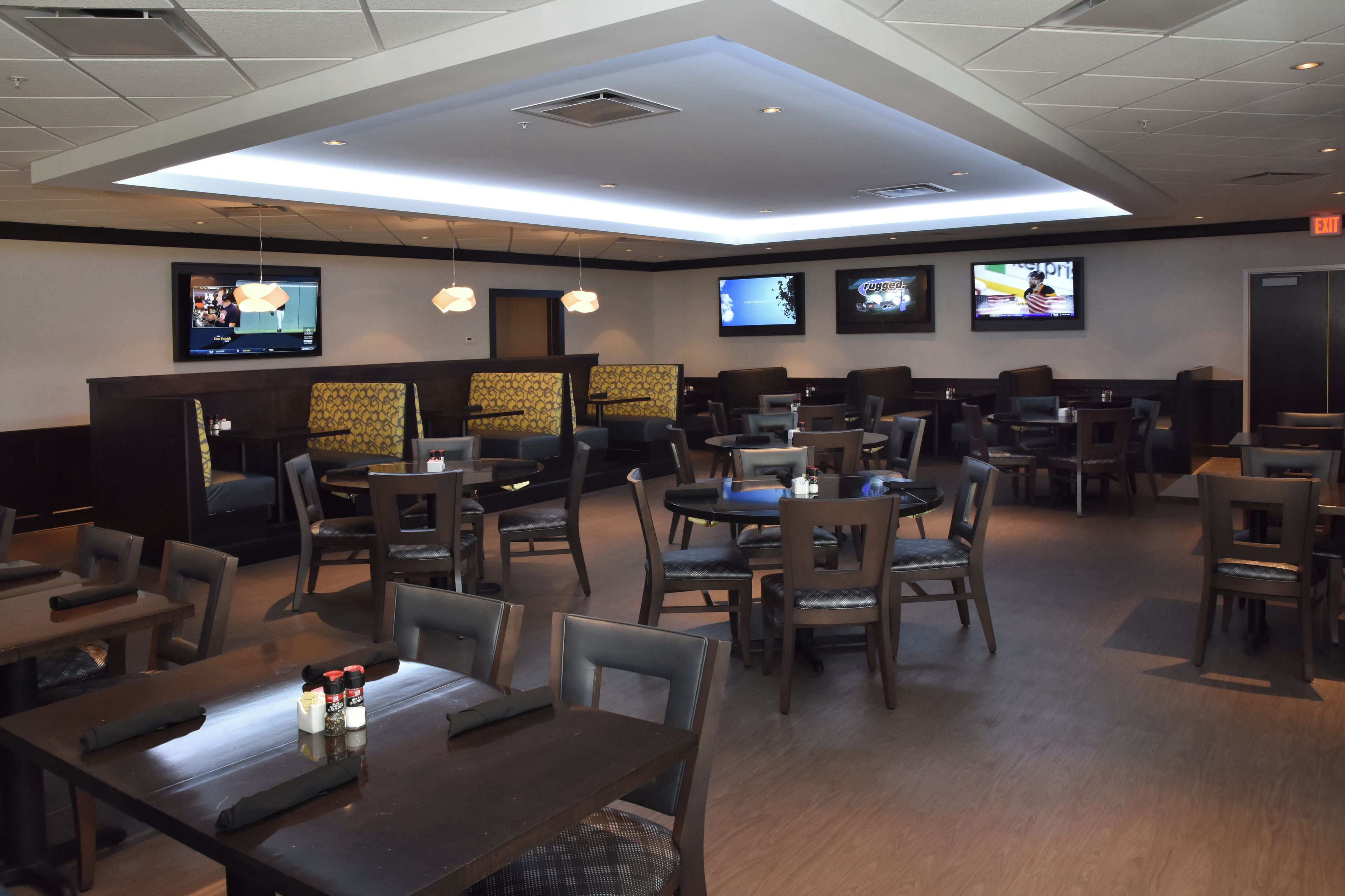 Un restaurante con varias mesas y cabinas, luces en el techo y televisores montados en la pared.