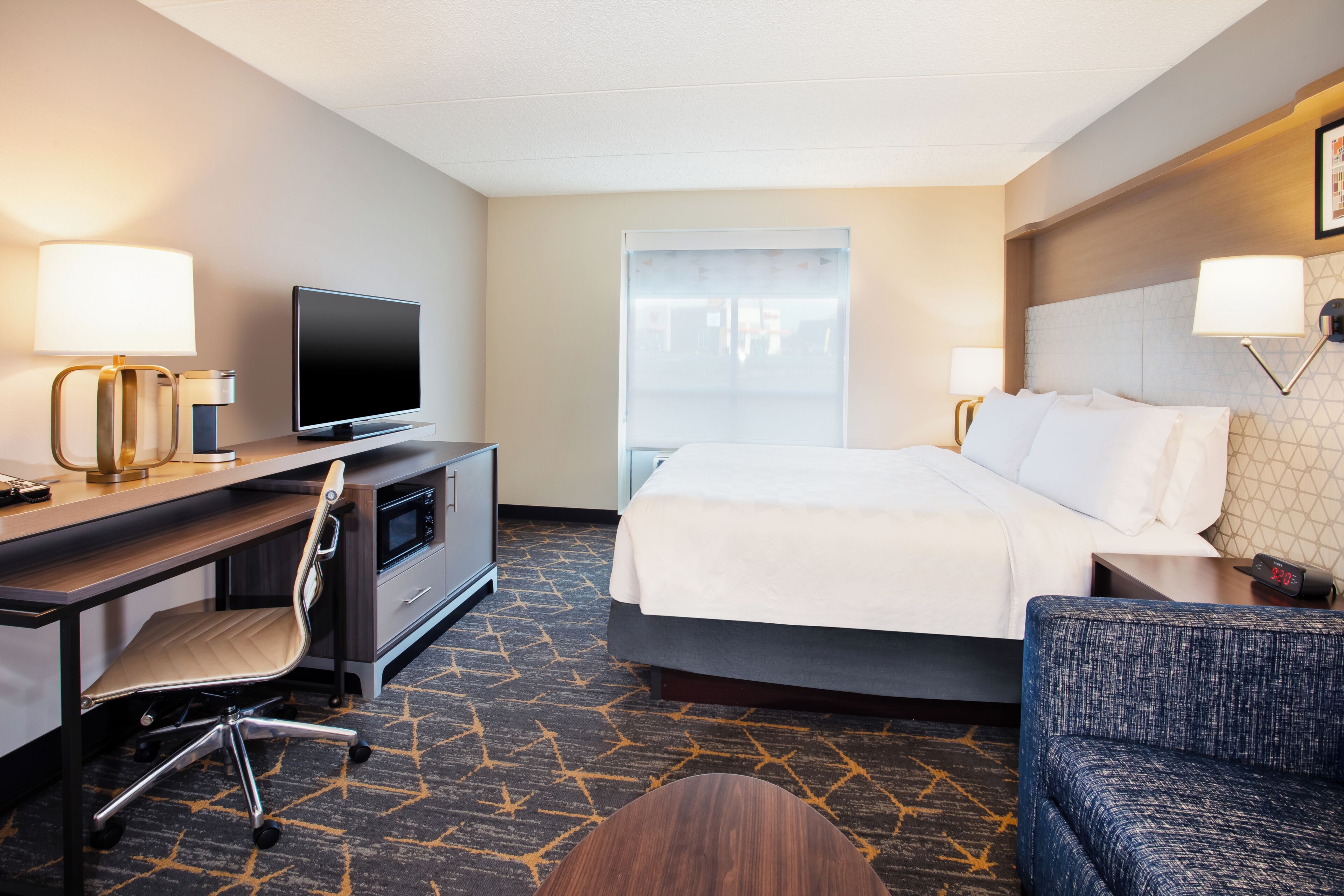 A hotel room with a bed, desk, chair, TV, and a window.