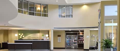 A spacious lobby with a reception desk, vending machines, and a large potted plant.