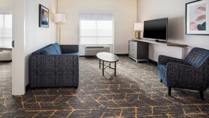 A modern hotel room with a sofa, armchair, TV, and a small table. - Holiday Inn Canton (Belden Village) by IHG (Canton)