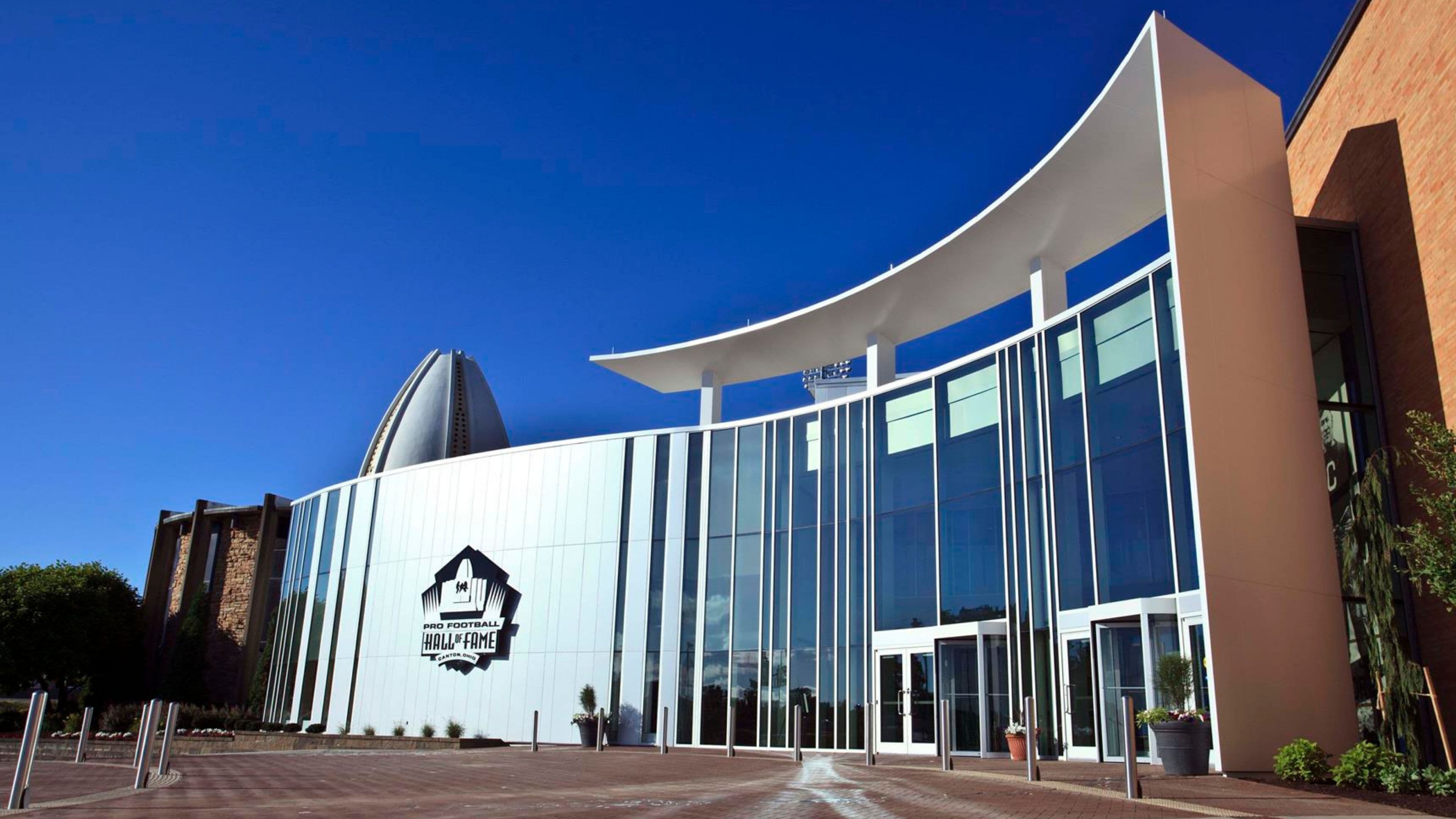 Un bâtiment moderne à la façade incurvée, doté de grandes fenêtres en verre et arborant un logo bien visible du Temple de la renommée du football professionnel.