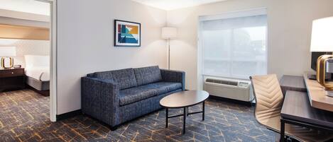 Habitación de hotel con sofá, una mesita redonda, lámpara, sillón y cama.