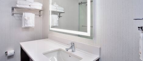 A bathroom with a white sink, a mirror, and shelves holding white towels.