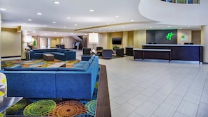 A modern lobby with a curved reception desk, a seating area with sofas, and a staircase leading to an upper level.