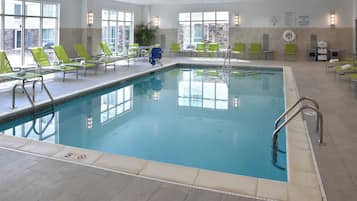 An indoor swimming pool with clear water, surrounded by green lounge chairs and a tiled floor.