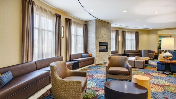 A hotel lobby with a brown leather sofa, patterned armchairs, a round coffee table, and a colorful patterned carpet. - Holiday Inn Canton (Belden Village) by IHG (Canton)