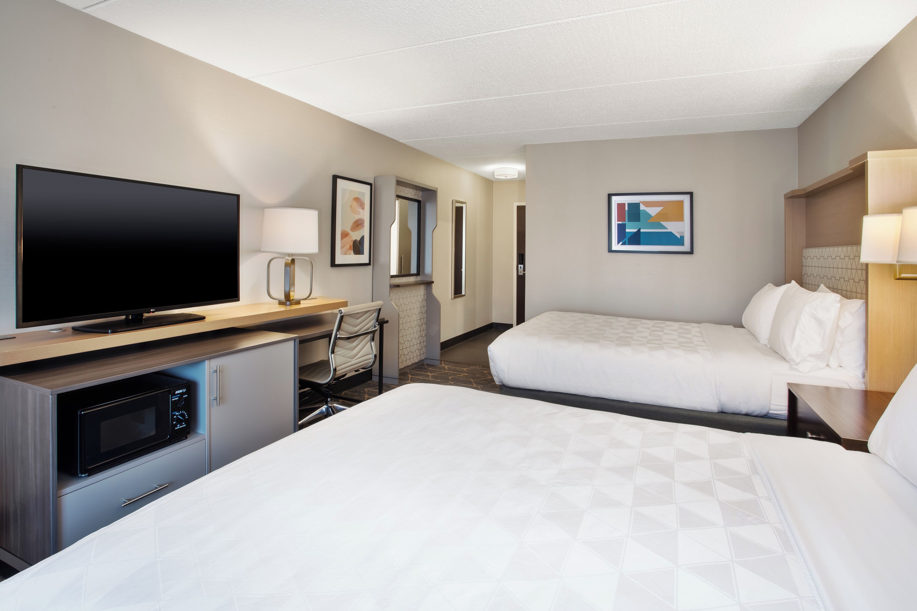 Een hotelkamer met een flatscreen televisie, een bureau met lamp, een stoel, twee bedden en kunstwerken aan de muren.