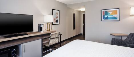 Ein Hotelzimmer mit einem großen Bett, einem Schreibtisch, einem Flachbildfernseher, einem Sessel, einer Mikrowelle und einem kleinen Schrank.