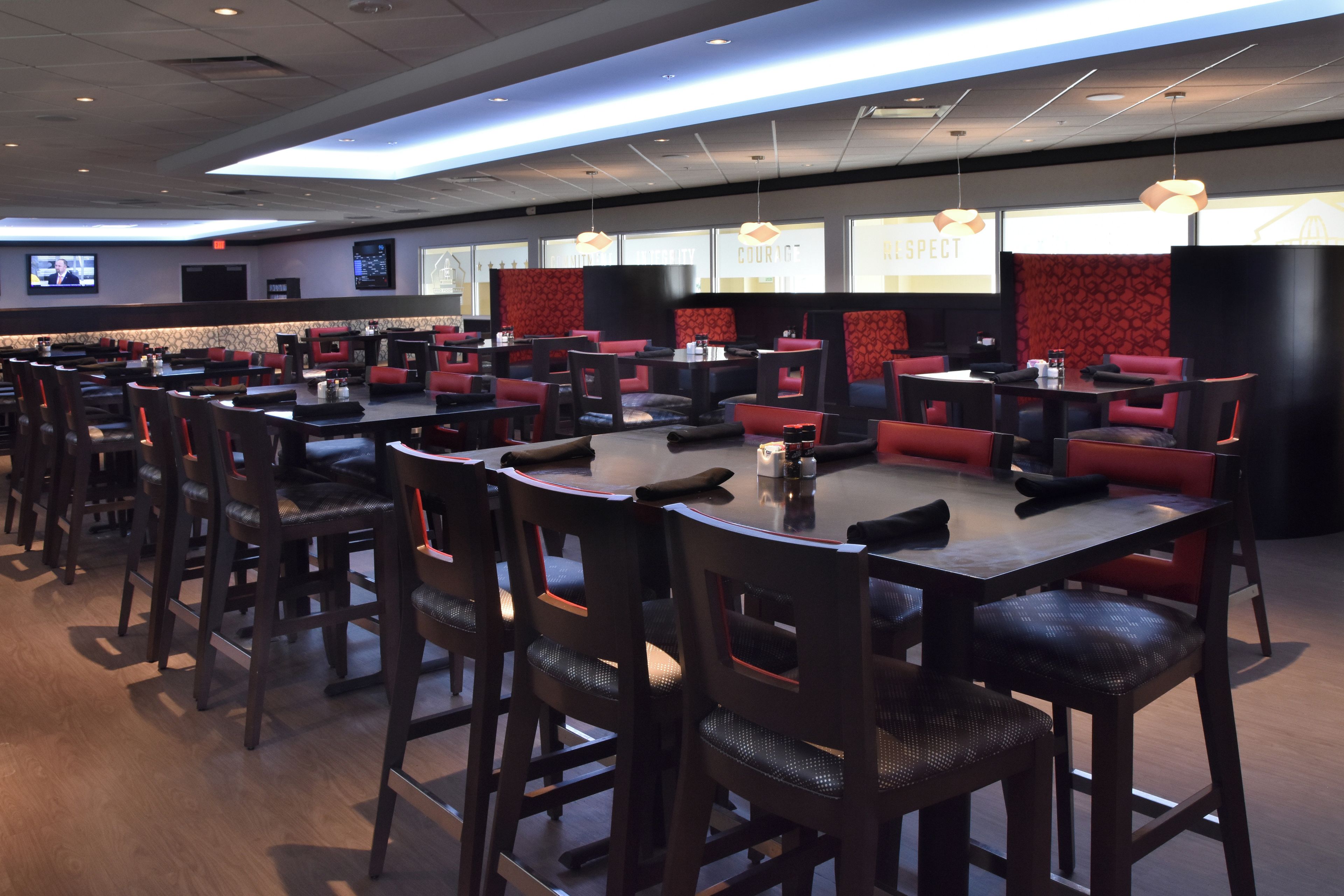 A spacious restaurant with multiple tables and booths, a flat-screen TV mounted on the wall, and a patterned red wall in the background.