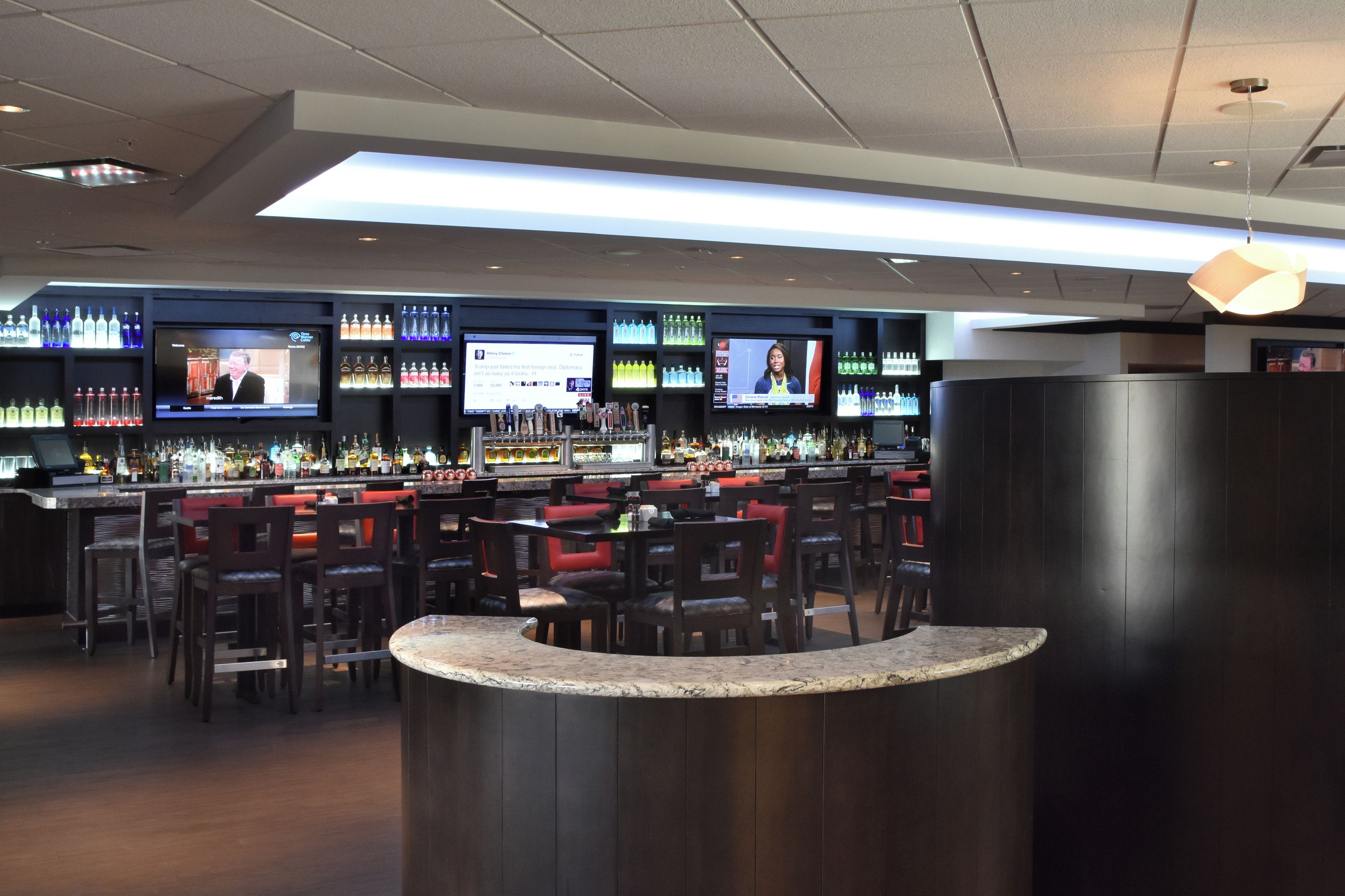 A bar area with multiple screens displaying content, a variety of liquor bottles, and seating arrangements.